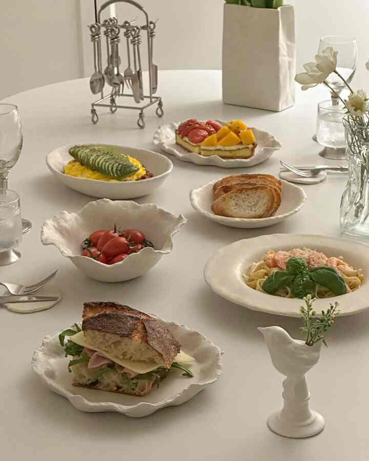白を基調としたダイニングテーブルに様々な皿とカトラリーが整然と配置されたシンプルな食事スペース