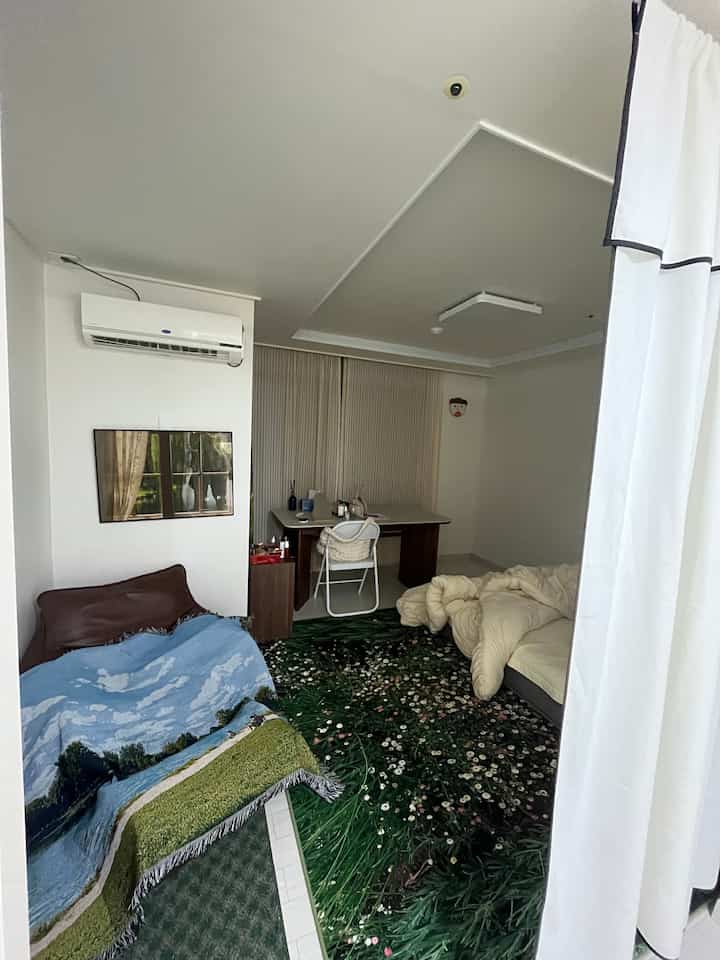 ナチュラルカラーとグリーンが際立つリビング、フラワーパターンのラグとシンプルなデスクやソファが配置された雰囲気のある空間