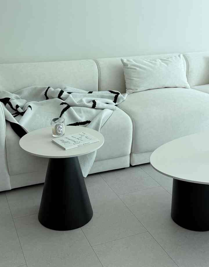 柔らかな白と黒のコントラストがあるモダンなリビング、丸いコーヒーテーブルとセクショナルソファが配置された印象的な空間