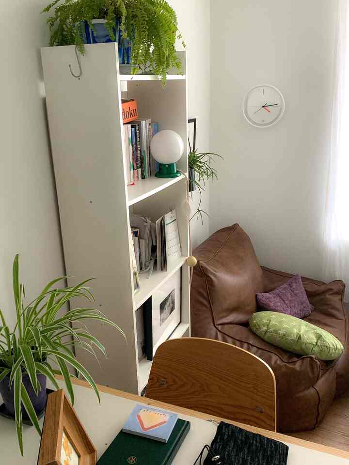 白い壁と本棚、茶色のビーズクッションソファと植物が配置された落ち着いた小さな部屋のインテリア