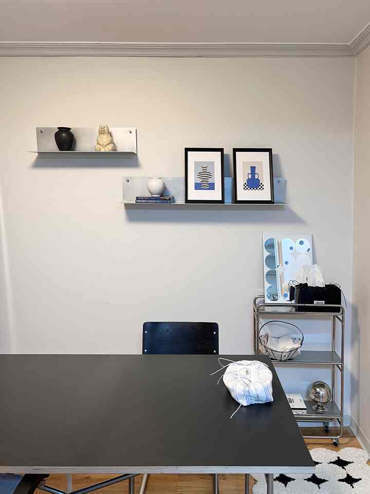 Modern dining room with white walls and black dining table, featuring metal shelves and picture frames
