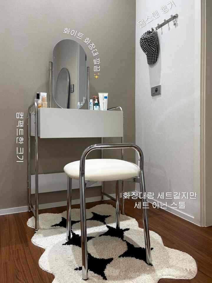 ホワイトとブラウンのトーンの狭い部屋、清潔感のある化粧台と独立したスツール、ブラックの星柄ラグが配置された印象的な空間