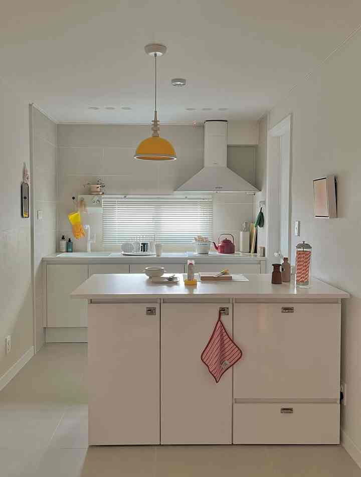 ホワイトのミニマルなキッチン、中央にキッチンアイランドと黄色のペンダントライトが配置された雰囲気のある空間