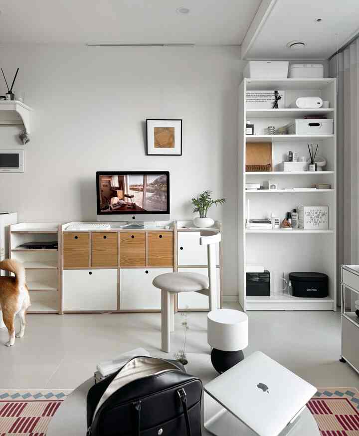 A white and wood-tone home office for a single occupant featuring a cabinet, computer desk, and minimalist decor with organized storage