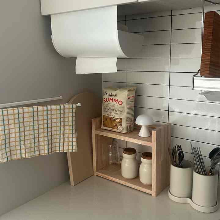 ナチュラルカラーのキッチンコーナー、木目調の棚と白いタイルの壁、整理されたキッチン用品が配置された落ち着いた空間