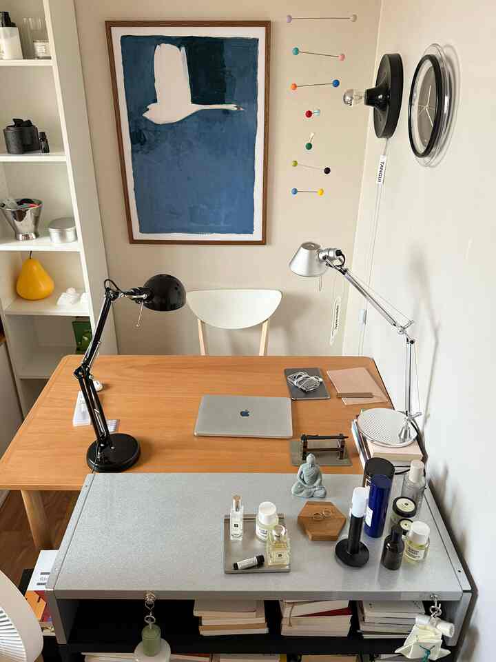 ナチュラルなブラウンとホワイトのトーンが調和したワンルームのホームオフィス空間。木製デスクとデスクランプ、壁掛け時計と絵画が配置されたシンプルで雰囲気のあるインテリア