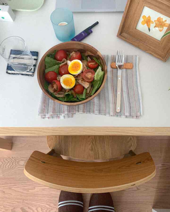 ホワイトテーブルの上にナチュラルな木目調の椅子とベージュのランチョンマットが配置された、おうちカフェ風の食事スペース