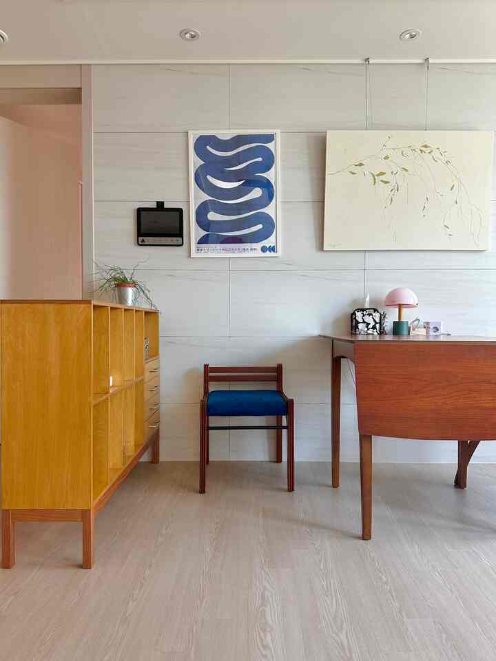 明るい木目調の床と家具、青い額縁のアートとヴィンテージ風のデスクが配置された清潔感のあるリビング