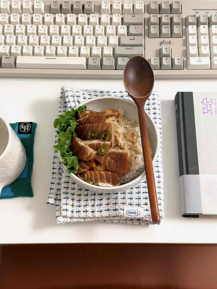 ホワイトテーブルにレトロなキーボードと白いご飯のボウル、木製スプーン、本が置かれた落ち着いた一人暮らしの空間