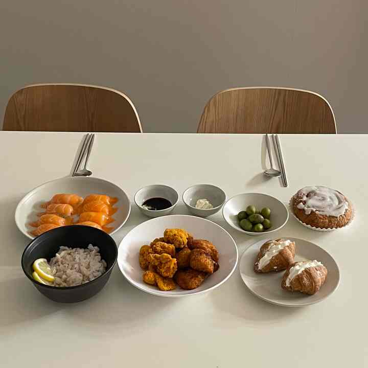 ナチュラルな色調のダイニングルーム、二脚の木製チェアと白いダイニングテーブルに様々な料理が整然と並べられた雰囲気のあるインテリア