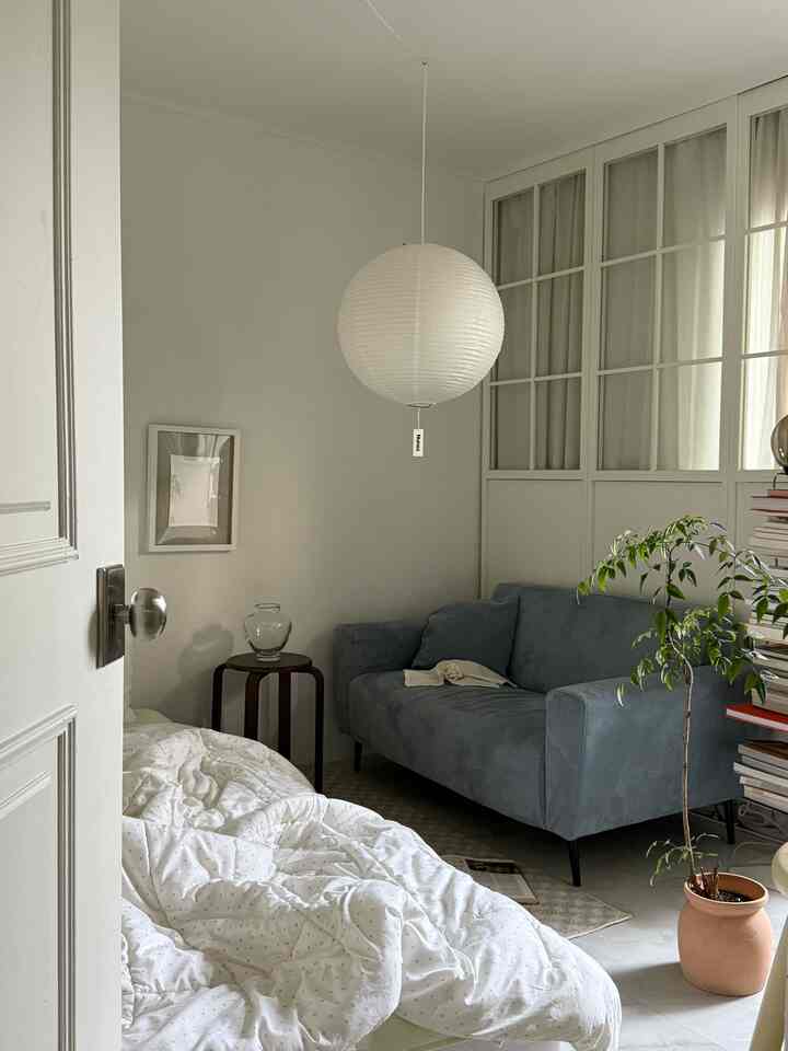 白とナチュラルトーンのリビング、青灰色のソファとペンダントライト、植物が配置された雰囲気のある空間