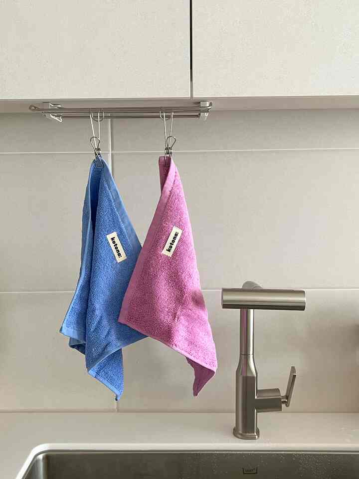 White-toned kitchen space featuring stainless steel faucet and pastel-colored towels hanging centrally, creating a clean look