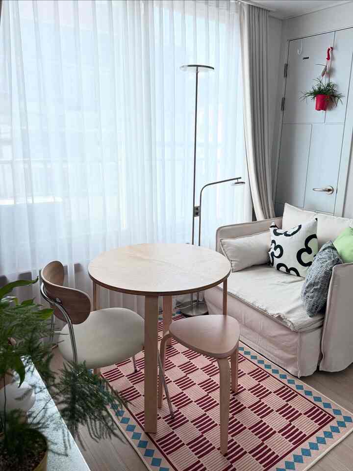 ベージュと赤のトーンが調和した狭いワンルームのリビング、丸テーブルとソファ、フロアランプが配置された明るく居心地の良い空間