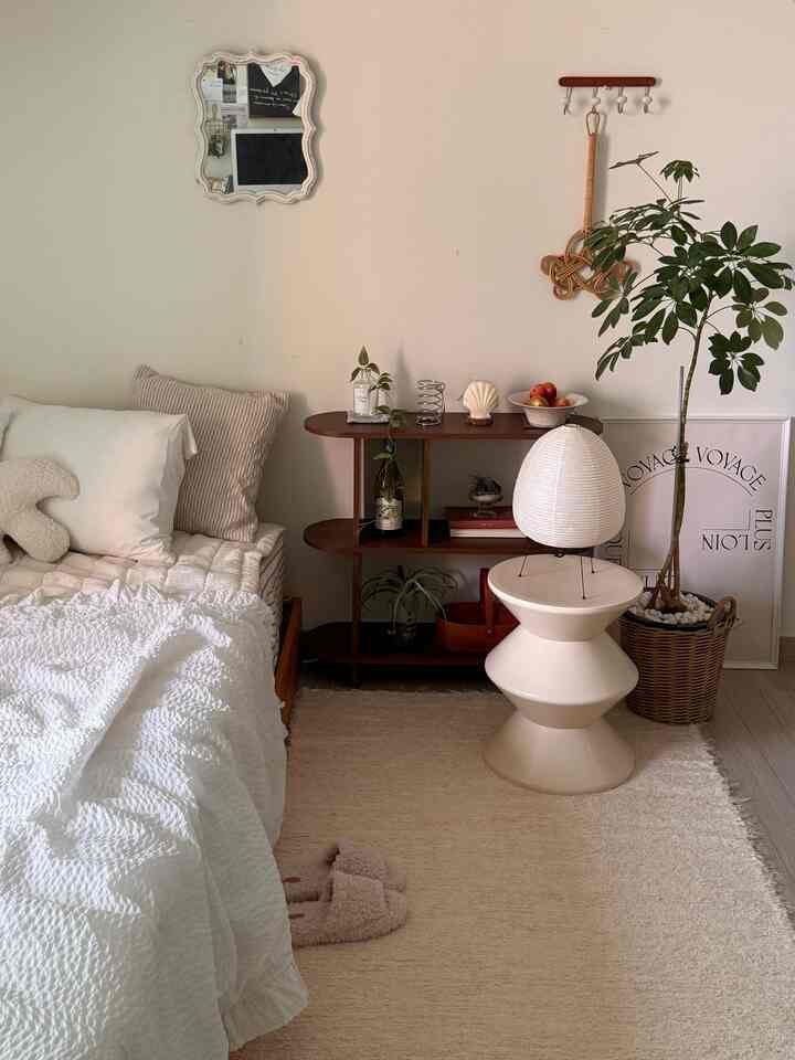 ホワイトとベージュの寝室、木製のサイドテーブルと植物が配置された落ち着いたナチュラルなインテリア