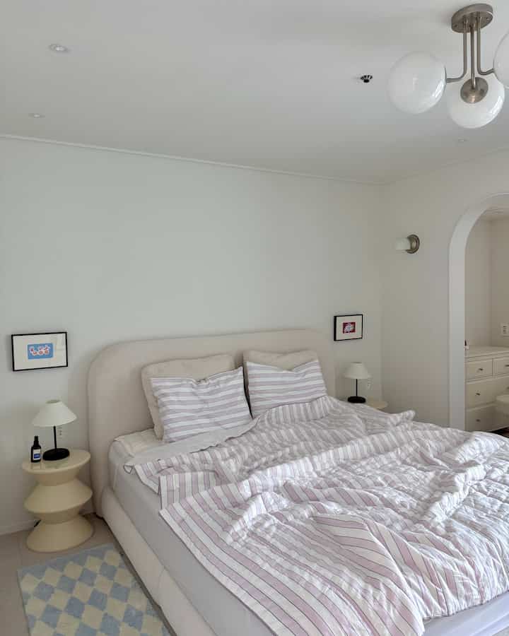 白とベージュの色調の寝室、中央にベッドと両側にナイトテーブルが配置されたシンプルで自然な雰囲気のインテリア