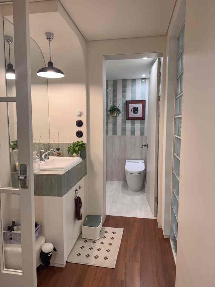 白とナチュラルカラーの細長いトイレ入口、ペンダントライトと洗面台が配置された清潔感のある空間