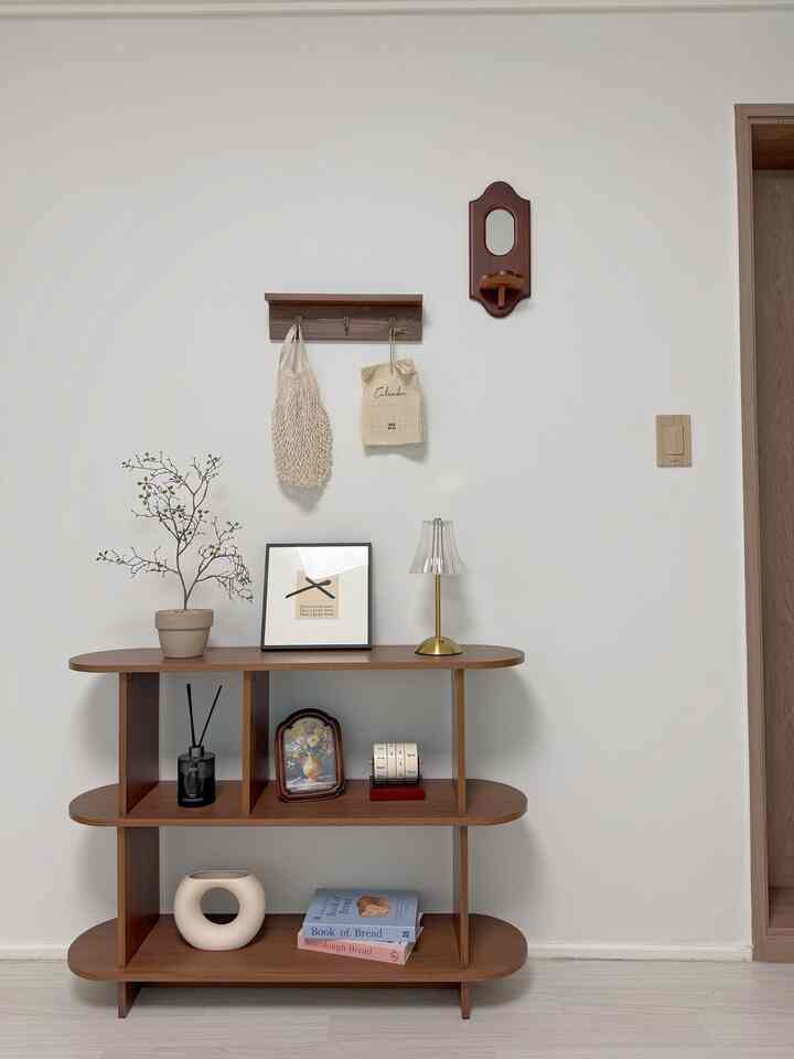 白い壁と木目調の3段棚が配置されたナチュラルテイストのリビング空間、ビンテージのオブジェや植物であたたかみのあるインテリア
