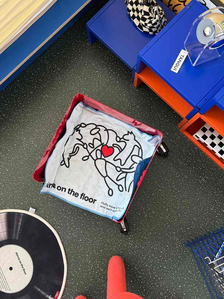 アイボリー色のペット用寝具が置かれた黒の斑点パターンの床と、青とオレンジの積み重ねシェルフが配置された雰囲気のあるインテリア