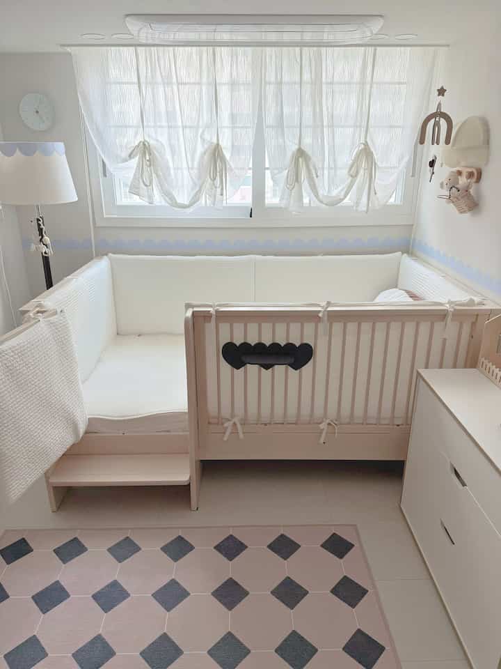 白と木目調が調和した赤ちゃんの部屋、ハート形の黒いアクセント棚と柔らかい布地が居心地の良い雰囲気を作り出す