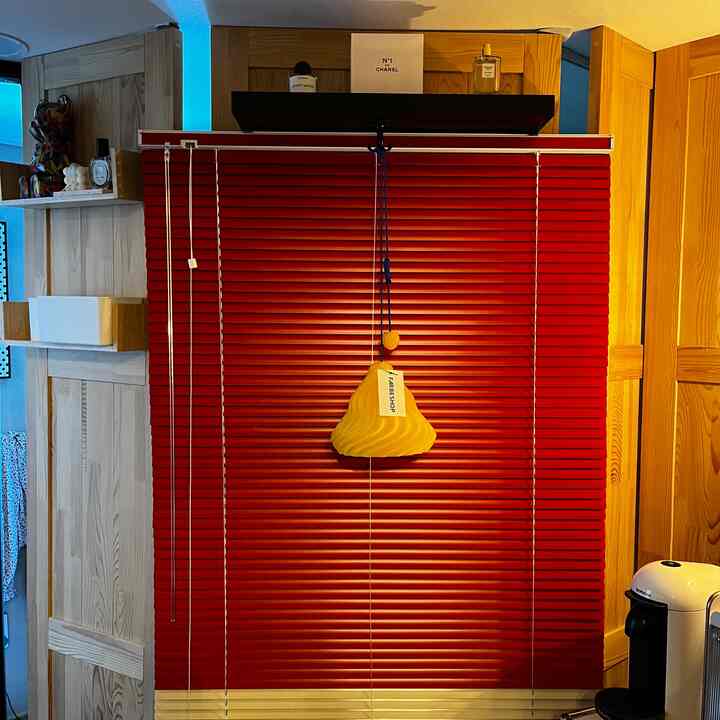 赤いブラインドと薄い木目調の壁が調和する印象的な空間、中央に黄色のペンダントライトがアクセントとして配置されている
