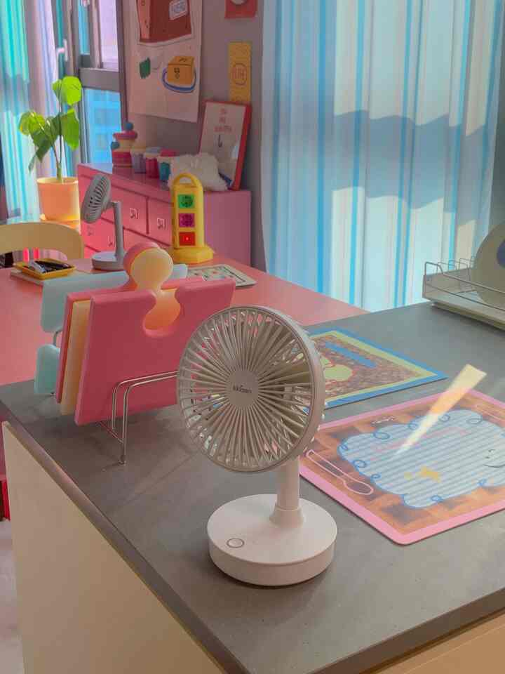 ピンクと白を基調としたキッチン、扇風機とキッチン用品が配置された明るく落ち着いたインテリア