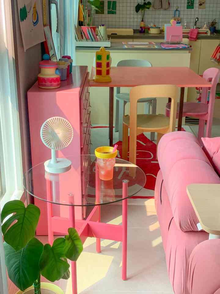 明るいピンク色の家具が配置された居心地の良いリビングとキッチン、自然光と透明なガラステーブルが印象的なインテリア
