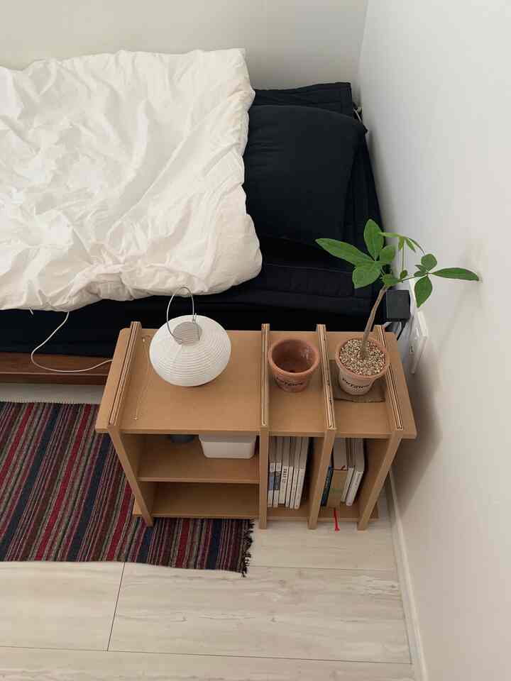 白とネイビートーンの寝室、ベッドとモジュール式の段ボール棚に植物が配置された、清潔でモダンな雰囲気のインテリア