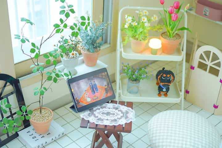 白とベージュのトーンの居心地の良いベランダ空間、様々な植物と小さな木製テーブルが配置され、雰囲気のあるおうちカフェを演出