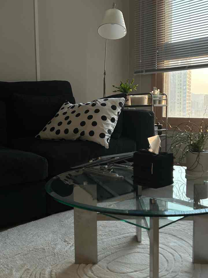 モノトーンのリビング、黒いソファとガラスのソファテーブル、移動式トロリーとフロアランプが配置された印象的なワークスペース