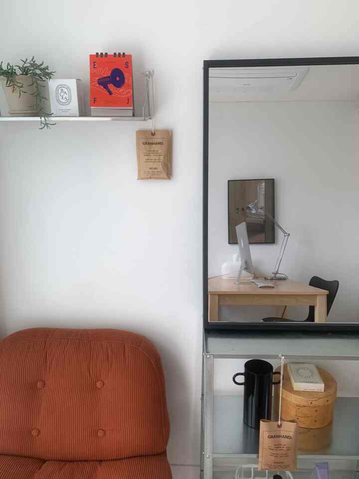 白い壁とブラウンのソファがあるワンルーム、ブラックフレームの壁掛け鏡とスチール製の壁棚が整った雰囲気を演出する空間