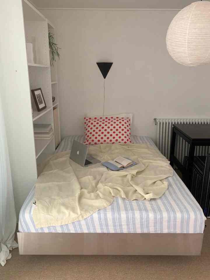 White and beige toned bedroom featuring a striped mattress, polka dot pillow, laptop and book on the bed creating a simple atmosphere