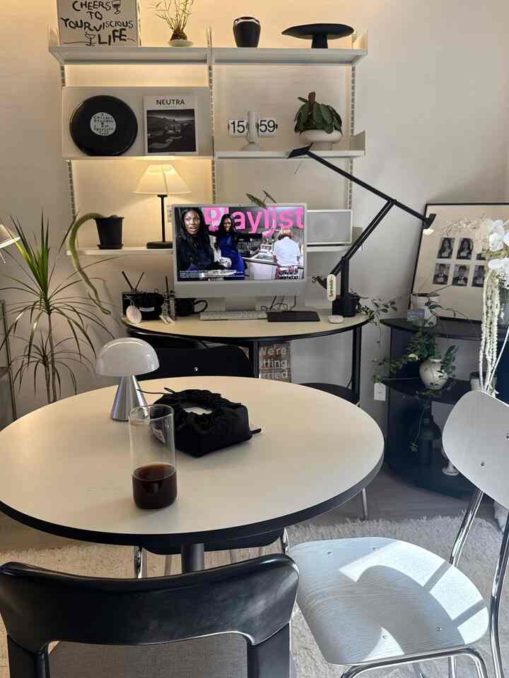 Modern home office space in white and black tones featuring a desk, round dining table, table lamps, and plants