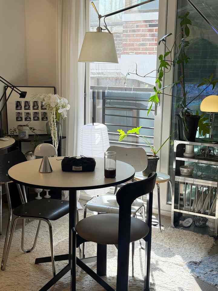 Bright white-toned dining room featuring a round dining table with four chairs and plants by the window, creating a natural modern atmosphere
