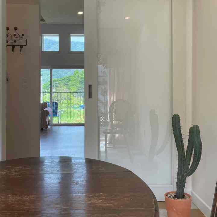 Bright white and brown-toned studio living room featuring wooden dining table and balcony with natural scenic view
