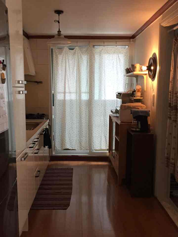 白と茶色のトーンでまとめられた狭くて居心地の良いキッチン、カーテンと収納が配置された実用的なレイアウト