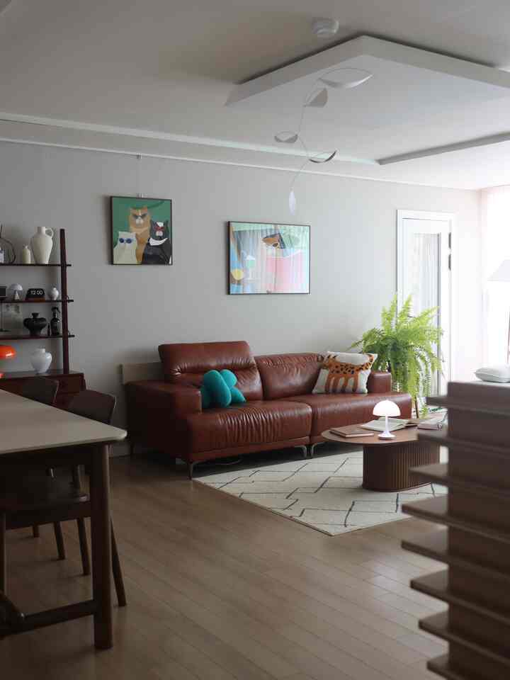 茶色のレザーソファと猫のポスターが配置されたナチュラルな色調のリビングインテリア。