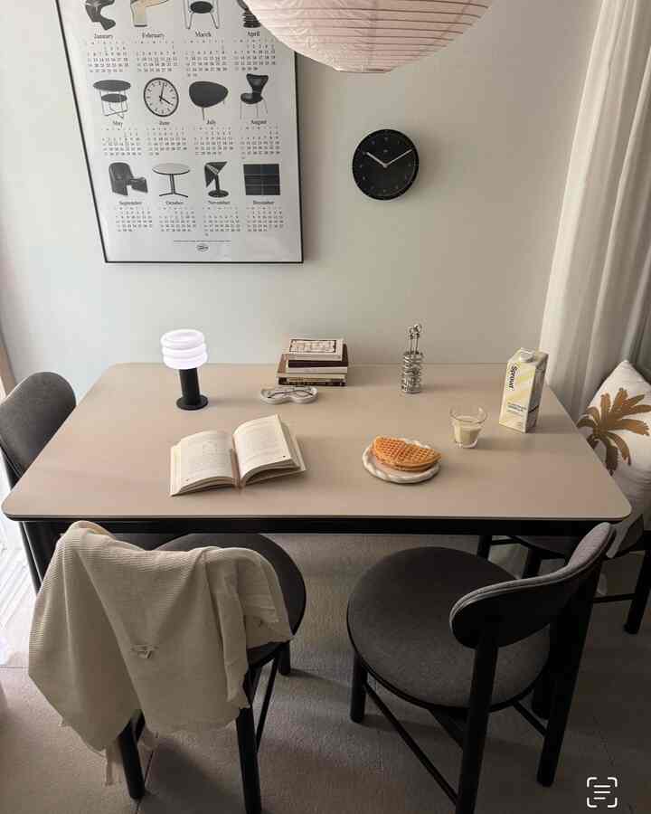 Beige and gray toned dining room featuring simple dining table, chairs, wall clock, and poster with calm atmosphere
