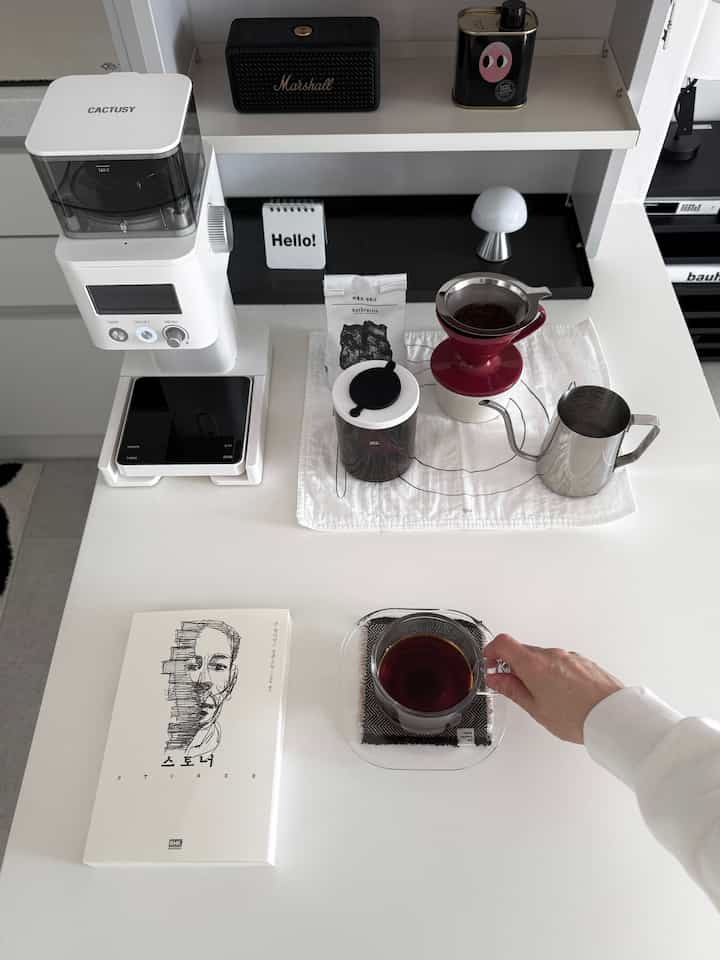 Monotone space featuring a white desk with home cafe coffee tools, book, and coffee cup in a modern atmosphere