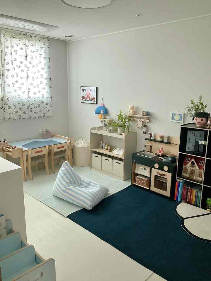 Natural toned kids' room featuring a small desk, bean bag, educational storage, and a play kitchen in a neat and cozy space