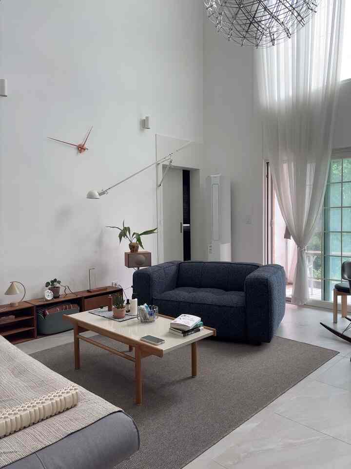 白い壁と高い天井のミニマルなリビング、ネイビーカラーのファブリックソファと木目調のコーヒーテーブルが配置された空間