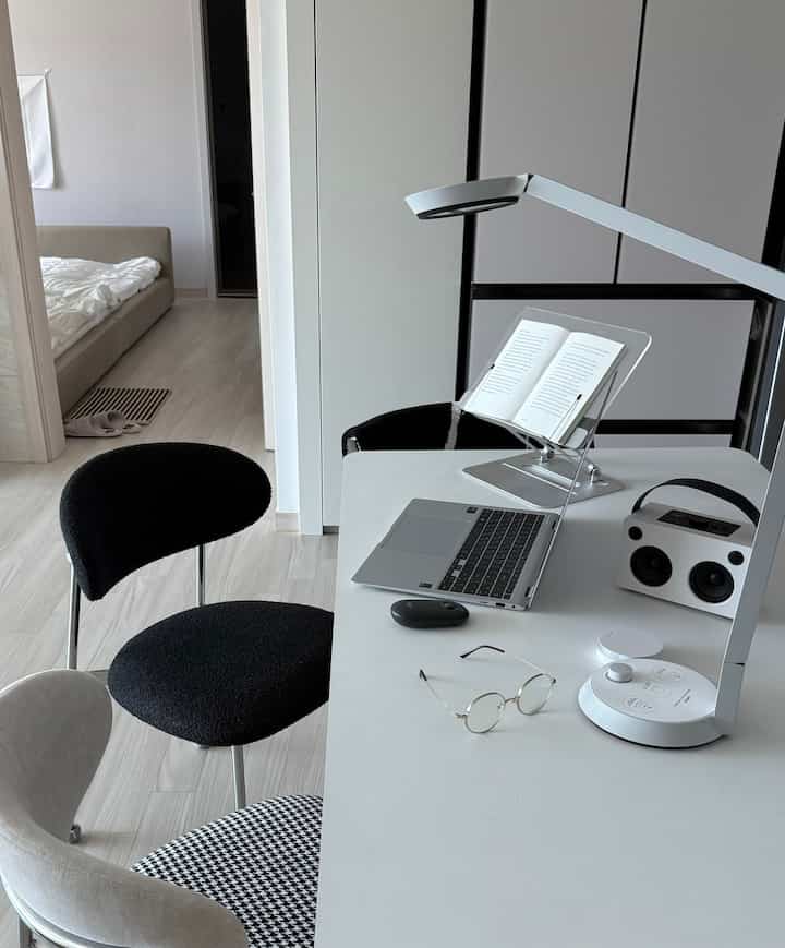 Monotone study and home office space featuring a white desk with laptop, book stand, and Bluetooth speaker in a clean setup