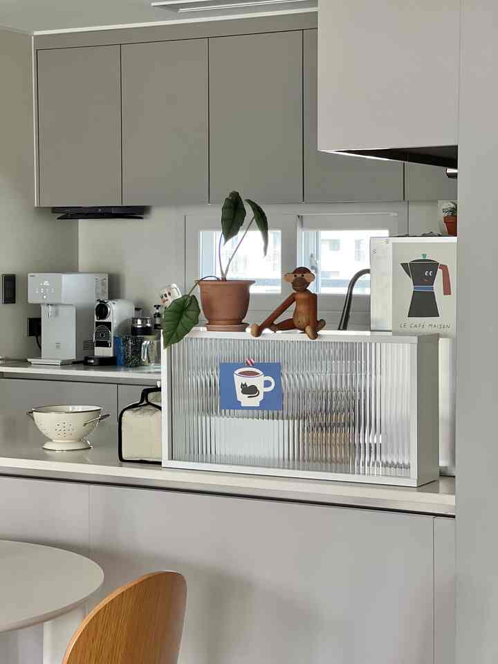 White and gray toned kitchen featuring a coffee machine, plant, and wooden decor in a clean, modern home cafe style