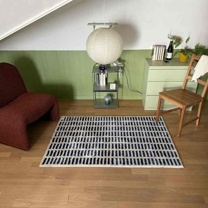 Natural-toned compact living room featuring a burgundy armchair, green dresser, and patterned rug in a cozy setting