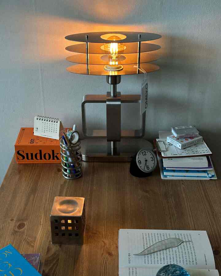 Natural brown tone desk featuring a silver table lamp, stationery, and clock arranged in a cozy, organized home office space