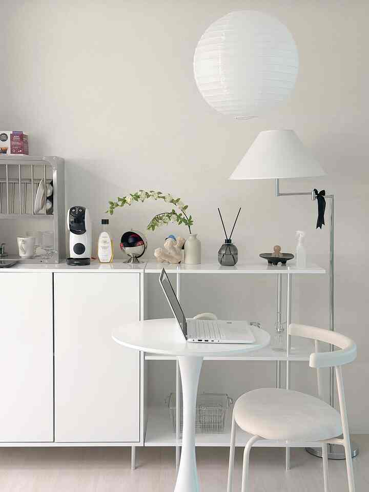 Modern compact home cafe space in white and natural tones featuring a round mini table, kitchen rack, and floor lamp.