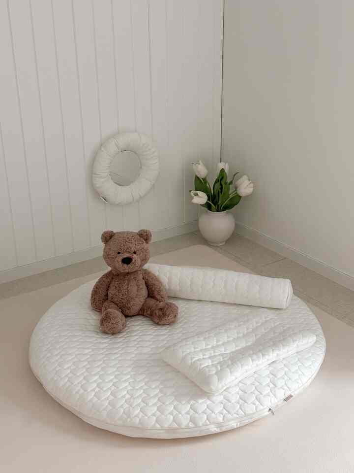 Natural white and brown toned kids' room featuring a round baby rug, cushions, and teddy bear creating a cozy space