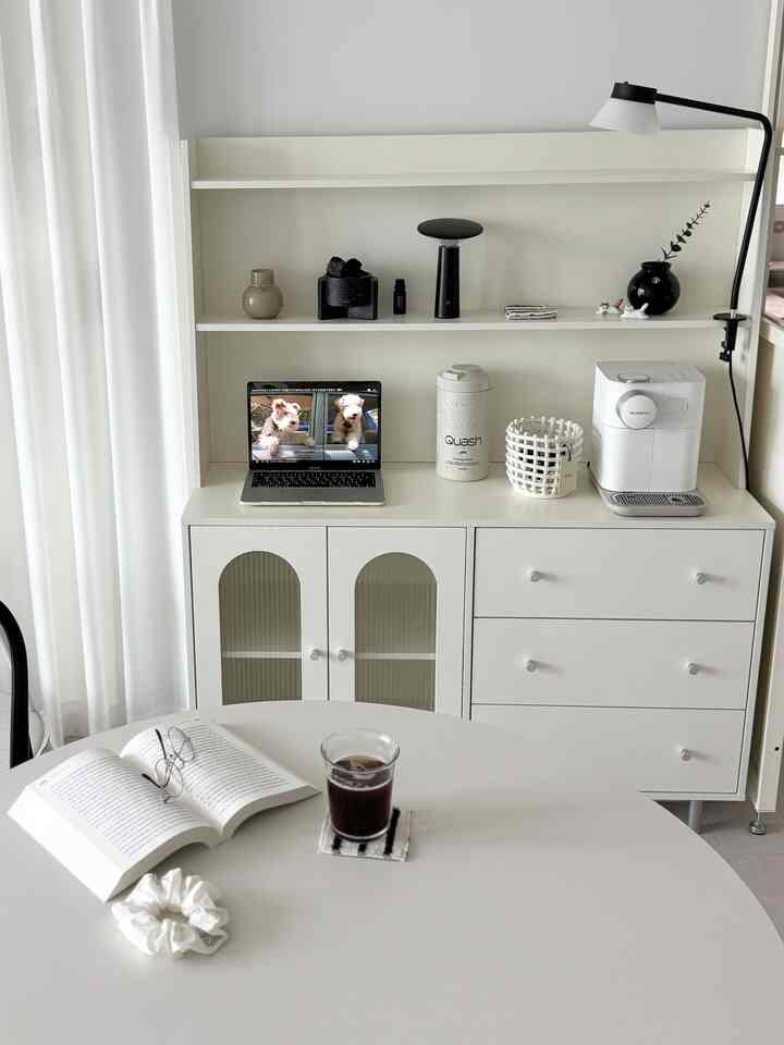 白を基調としたキッチン兼おうちカフェ空間、丸テーブルとコーヒーマシン、収納キャビネットが整然と配置されたモダンなインテリア