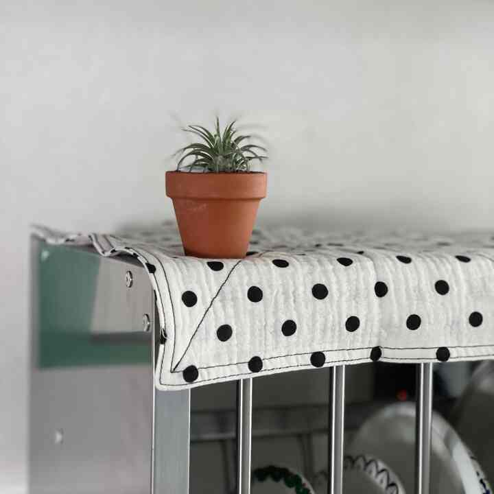 白いポルカドットのテーブルマットの上にテラコッタ鉢が置かれたステンレス製のキッチンラックが配置されたモダンなキッチンの空間