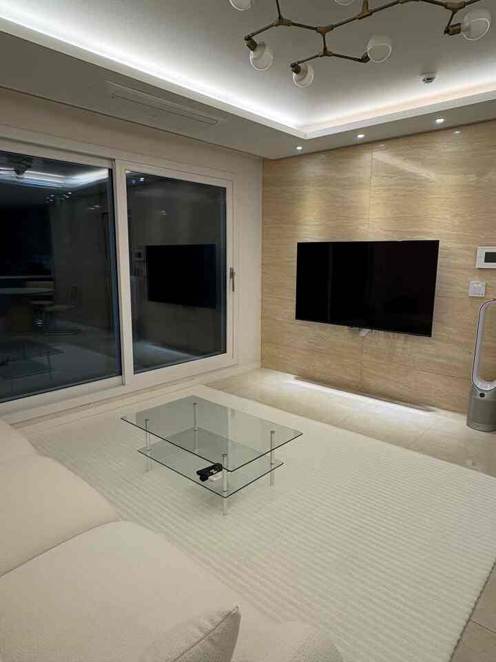 白とベージュのトーンのモダンなリビングルーム、強化ガラステーブルとシンプルなソファが配置された清潔で整った空間