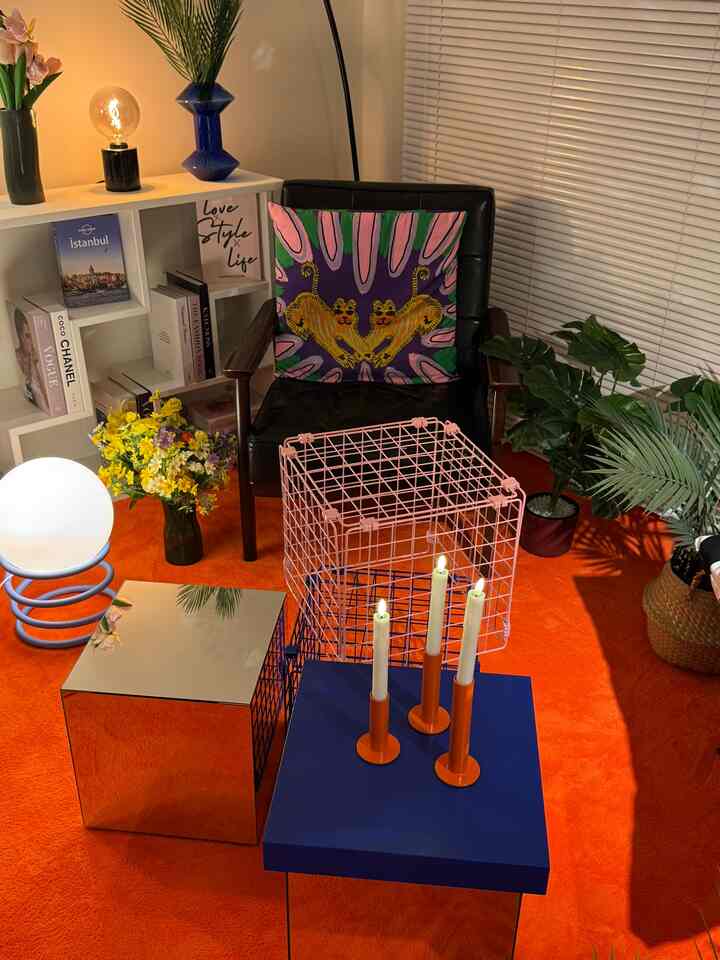 A modern living room with an orange rug, featuring a black armchair with an art cushion at center and a blue table with orange candle holders creating a cozy atmosphere